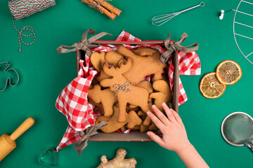 Top view of childs hand reaching freshly backed Christmas gingerbread cookie deer form over green...