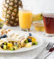 Tropical fruit crepes surrounded by juice, tea and fruit ready for eating.