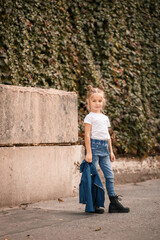 Stylish blonde little girl in jeans and a white T-shirt walks down the street. Girl 7 years old small model, beautiful child