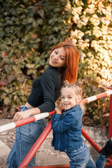 Fototapeta na wymiar Stylish red-haired mother and her daughter are talking warmly. Happy child and her mom on the street. Successful single mother with her daughter for a walk. Warm family relationship