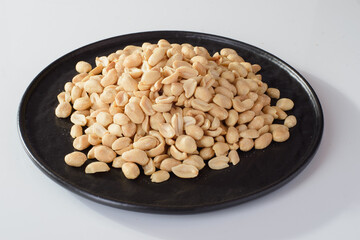 roasted salty peanuts on a round plate, beer snack isolated on white background