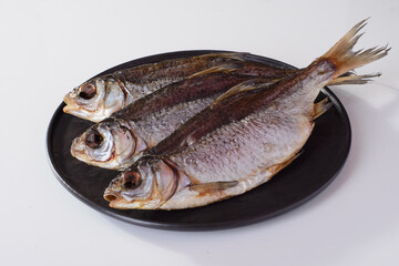 dried roach fish on a round plate, beer snack isolated on white background