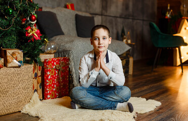 Beautiful boy sitting on floor next to Christmas tree. Family holidays