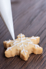 Close up of drawing Christmas snowflake sugar cookie on wooden table background with icing.