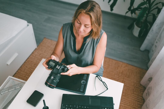 A young woman photographer sitting at his Desk and working with a camera. View from the top