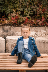 A beautiful little girl is sitting in stylish clothes on wooden pallets. Stylish child in a blue jacket. Casual style, fashion for children, fashionable suit, happy childhood