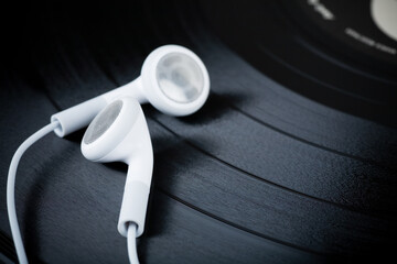 Two white earbuds on a black vinyl record.
