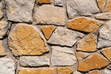 A wall built of wild stone. Mosaic of stone. Stone abstraction. Beige and brown tones with shadows. Background texture used for interior or exterior design, ancient and grunge rocks of different shape