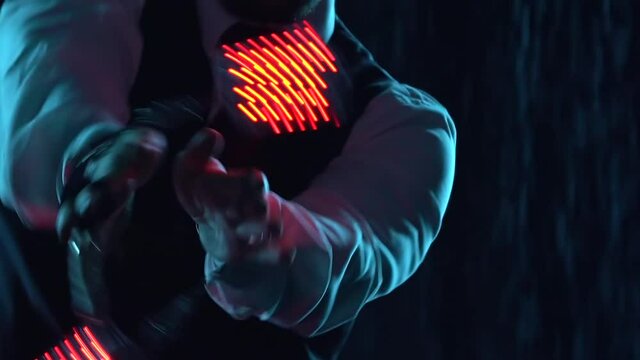 A professional circus artist performs tricks with a glowing grenade. Stylish man performs in the rain on a dark studio background. The artist's hands close up. Night performance. Slow motion.