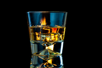 Whiskey or bourbon in a transparent glass with ice cubes on a black background with fire.