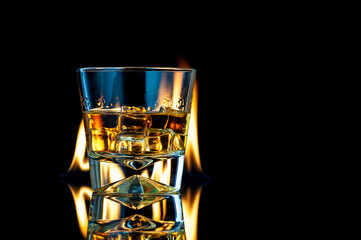 Obraz na płótnie Canvas Whiskey or bourbon in a transparent glass with ice cubes on a black background with fire.
