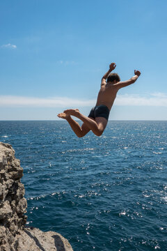 A young man jumping from a cliff into the sea. Vertical image.