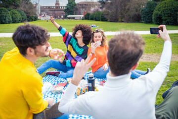 Four young students multi ethnic friends outdoor doing pic nic in a park using smartphone