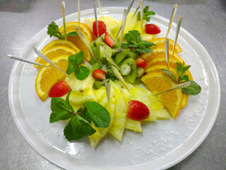 on a white plate, sliced ​​oranges, pineapple, kiwi and strawberries, all decorated with mint sprigs