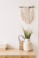 Bohemian concept in stylish interior of living room with flowers in vase, wooden desk, beige macrame, books and elegant accessories. Design home decor.