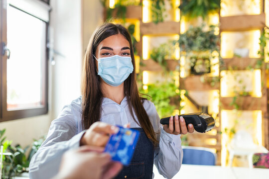 Waitress holding credit card reader machine and wearing protective face mask with client holding credit card. Man hand of customer paying with contactless credit card with NFC technology.