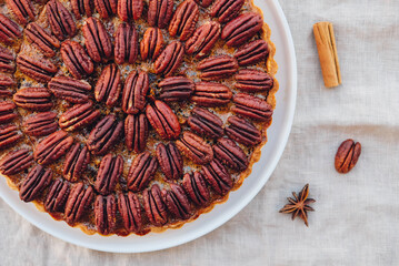 Delicious freshly baked homemade pecan pie on white tablecloth, close up. Sweet food from above. Popular holiday meal for Thanksgiving and Christmas.