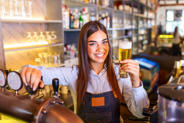 Beautiful smiling female Bartender serving a draft beer at the bar counter , shelves full of bottles with alcohol on the background