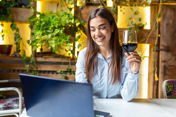 Woman works with glass of red wine and laptop in cafe. Woman using laptop while having wine at restaurant. freelancer