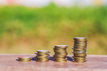 row of coin stack on wood table with blur nature park background. money saving concept for financial banking and accounting.