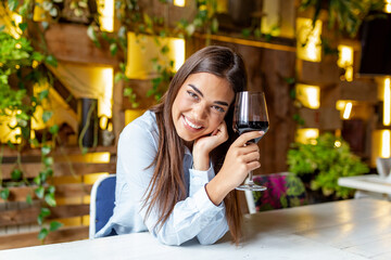 Image of cute pretty young woman sitting in cafe holding glass and drinking wine. portrait of a beautiful wine tasting tourist woman.