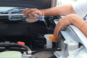 Women refills windshield wiper water on a car.