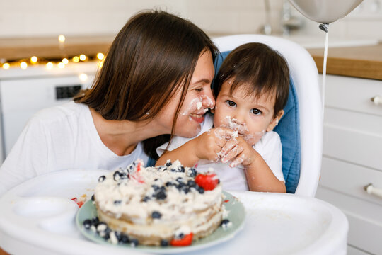 Happy mother with one year old baby celebrating with first birthday with white kitchen on background - Powered by Adobe