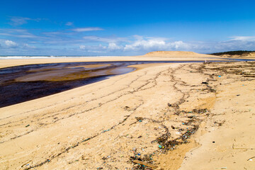Plage en plan large polluée par des déchets plastiques, au débouché de l'estuaire d'un fleuve...