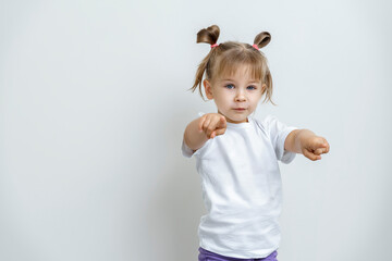 a cute little girl in a white t-shirt points her hands forward at the viewer. the concept of children's emotions. space for text and copy space