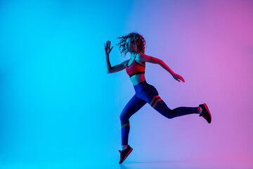 Runner. Young sportive woman training isolated on gradient blue-pink studio background in neon light. athletic and graceful. Modern sport, action, motion, youth concept. Beautiful female practicing.