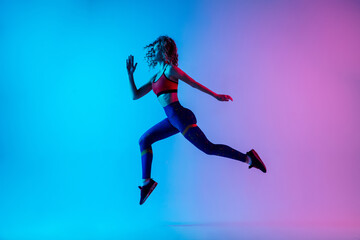 Obraz na płótnie Canvas Runner. Young sportive woman training isolated on gradient blue-pink studio background in neon light. athletic and graceful. Modern sport, action, motion, youth concept. Beautiful female practicing.