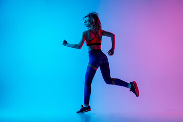 Fototapeta na wymiar Runner. Young sportive woman training isolated on gradient blue-pink studio background in neon light. athletic and graceful. Modern sport, action, motion, youth concept. Beautiful female practicing.