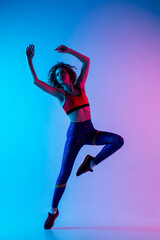 Jump. Young beautiful woman in bright sportwear isolated on gradient pink-blue background in neon light. Athletic and graceful. Modern sport, action, motion, youth concept. Sportive female practicing