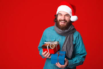 Handsome bearded man holding gift boxes over red background and looking happy at camera