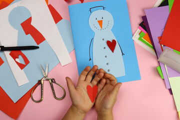 Fototapeta na wymiar The child makes a Christmas card on the table of the house, applique snowman