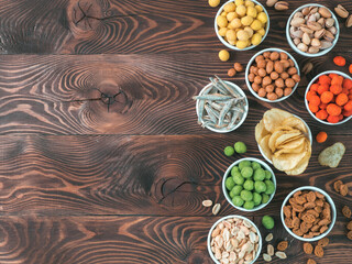 Assortment of different snack for beer, wine, party. Peanuts in coconut glaze, green vasabi, red spicy chilli, yellow cheese glaze, chips, pistachio, crackers, fish on brown wooden table. Copy space