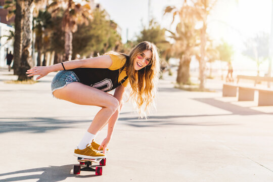 Skater girl riding a long board skate. Cool female urban sports. California style outfit. Woman on skateboard wearing pink glasses