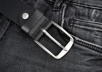 Black leather belt on denim. Jeans belt. Fastened fashionable men's leather belt with dark matted metal buckle isolated on white background. Black belt for men. Male accessory.