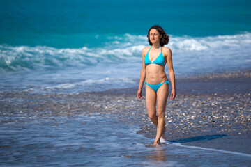 A woman in a swimsuit is walking along the sea waves.