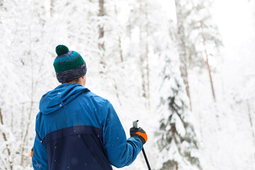 Skier in windbreaker and hat with pompom with ski poles in his hands with his back against the...