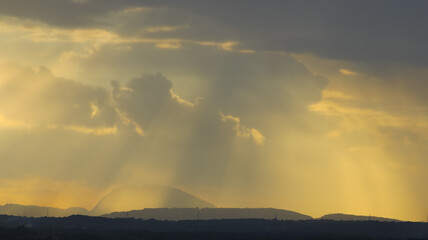 Silhouette of a hills against beautiful golden hour light and beautiful clouds formation with rays of sunlight breaking
