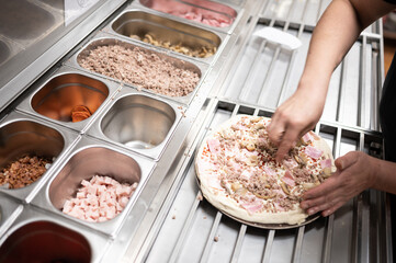 Chef adding ingredients to a pizza at small business.Top view Fast food take-away concept