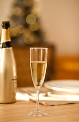 Christmas table setting with holiday decorations in a gold color. New Year celebration. A bottle and glass of champagne.