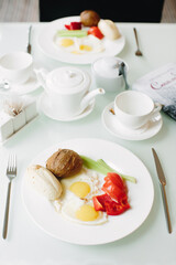 Breakfast for two. Fried eggs with vegetables and bread for breakfast. Table setting in white. Selective focus.