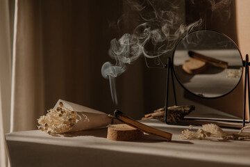  palo santo with jet of smoke, mirror and dried flowers on a neutral background. Abstract trendy...