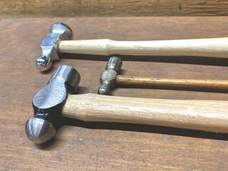 An artisan jeweller workshop with jewelry making tools. Three high quality metal chasing hammers with wooden handles, new and vintage.