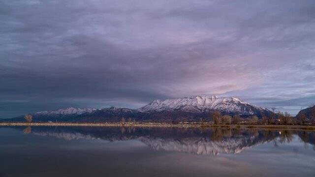 Time lapse of colorful sunrise reflecting in Utah Lake in Provo with snow capped Timpanogos Mountain in the distance.
