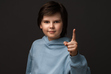 Portrait of Serious boy showing index finger. Studio shot, gray background. Human emotions, facial...