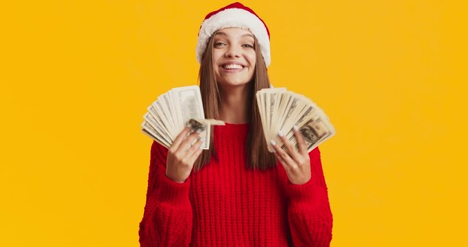 Pretty woman in red sweater and Santa hat holding money banknotes, ready to buy Christmas presents