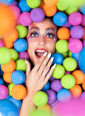 Fototapeta na wymiar Woman lying between colored balls, pleasantly surprised with her hand over her mouth. Happy surprise concept. Selective focus.